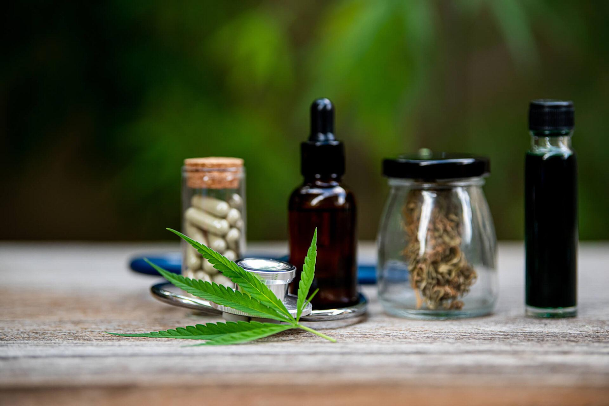 Hoja de cannabis con varias formas de consumo, como tinturas de aceite, flor seca, cápsulas y cartuchos de vape