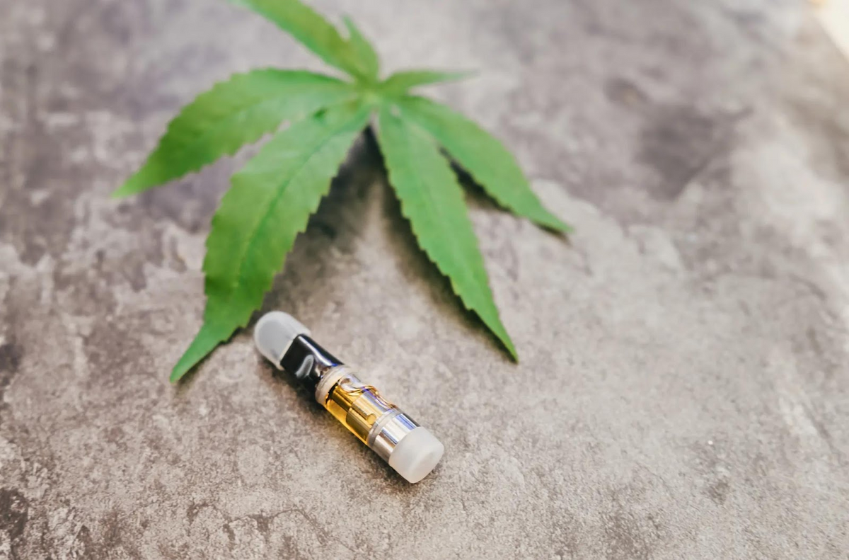 Hoja de cannabis y cartucho de vape sobre superficie de hormigón