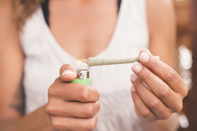 Persona sosteniendo un joint encendido con un mechero verde en una escena lifestyle